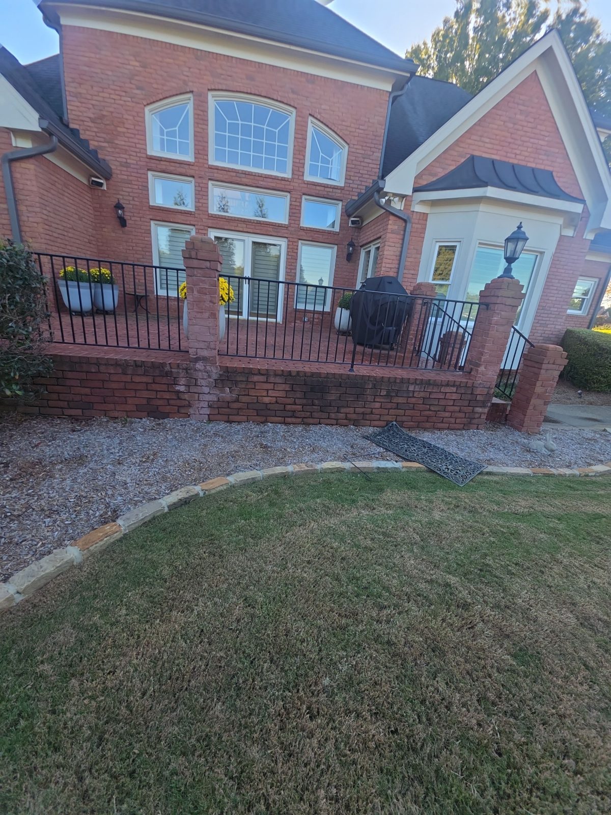 Raised red brick terrace and steps in Thornberry before cleaning, dark with mildew, with black iron railings above the landing