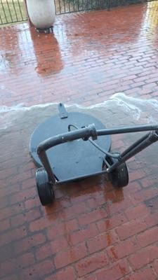 Round surface cleaner with a blue deck and metal housing on the Thornberry brick patio while the brick behind it is still dark with mildew