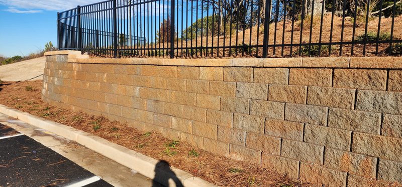Block retaining wall topped with black metal fencing beside a landscaped parking area