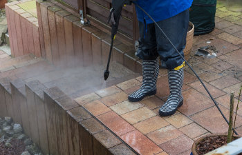 Woman cleans stone slabs with a pressure washer